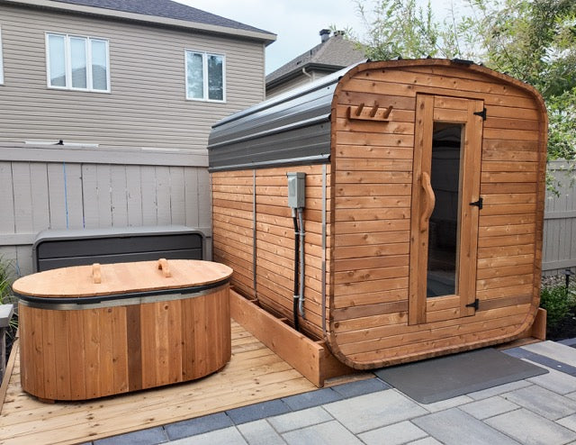 Cube cedar outdoor sauna beside a matching cedar cold plunge on a backyard patio, modern wellness setup in a residential outdoor space