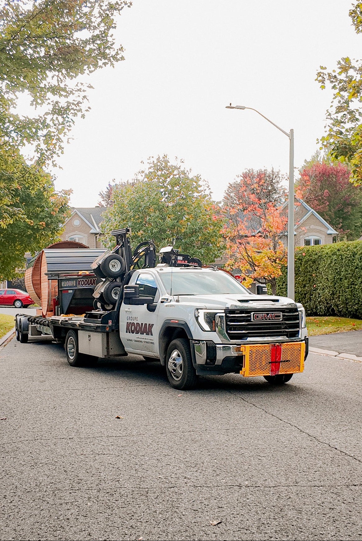 Kodiak Saunas delivery truck towing a trailer loaded with outdoor cedar saunas on a quiet residential street