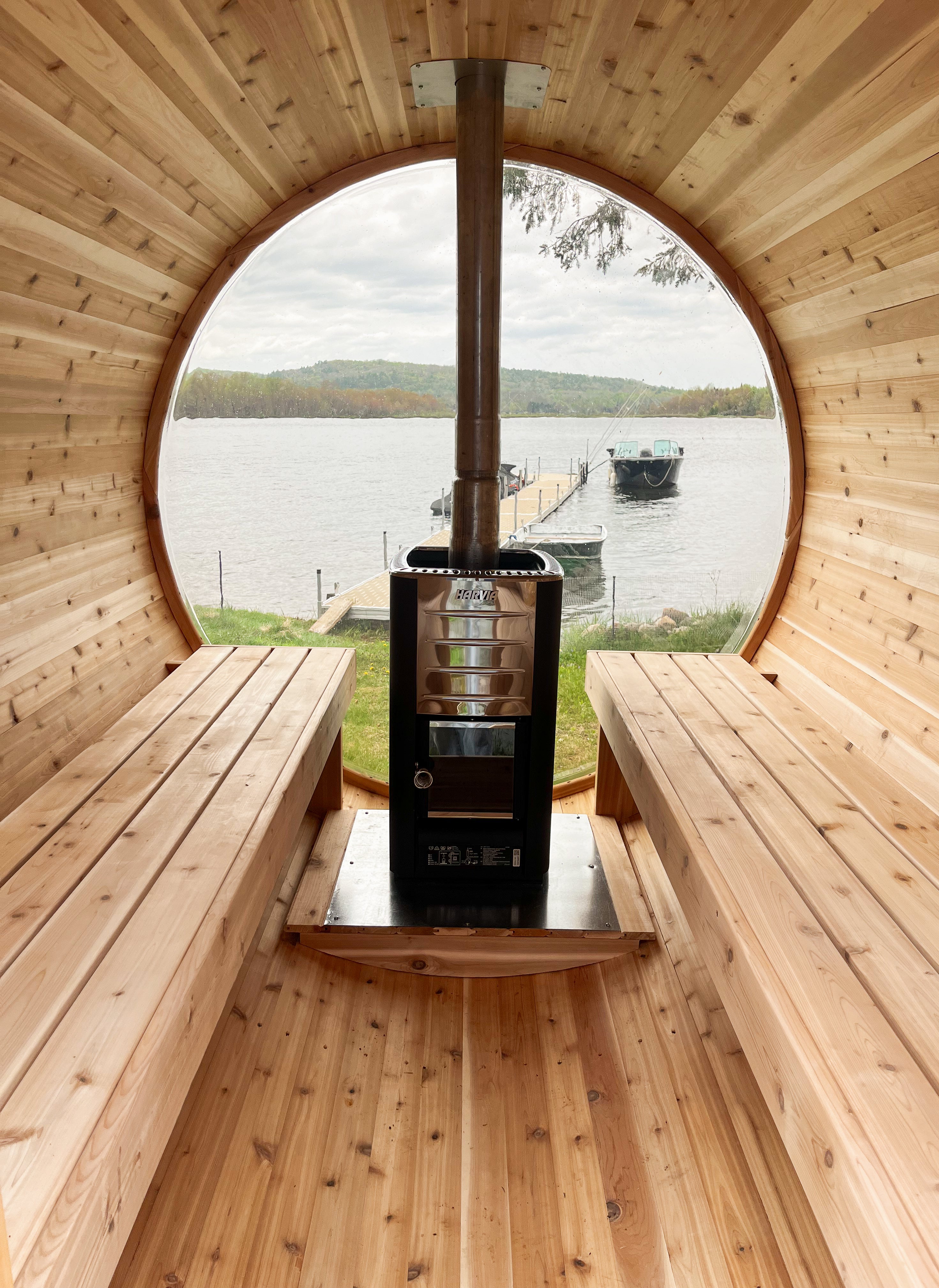 Harvia M3 wood-burning sauna stove installed inside a red cedar barrel sauna with panoramic window overlooking a lake, scenic outdoor sauna setting
