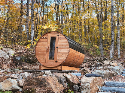 8-ft red cedar barrel outdoor sauna with black metal roof set on a rock ledge in a forest landscape, natural off-grid sauna setting