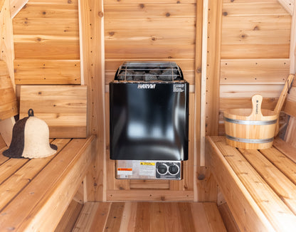 Close-up view of Harvia KIP electric sauna stove wall-mounted inside a cedar barrel sauna with wooden bucket, ladle and wool sauna hat beside the heater