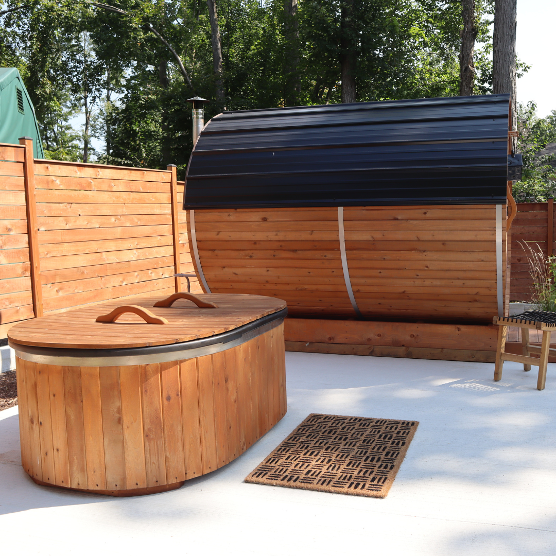 Cedar cold plunge tub beside a red cedar barrel outdoor sauna on a backyard patio, outdoor wellness and contrast therapy setup