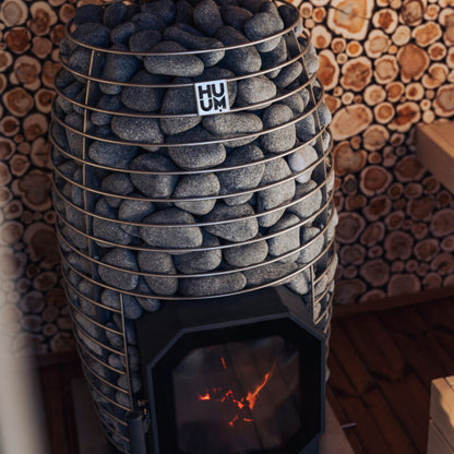 HUUM Hive Flow Mini wood sauna stove installed inside a cedar sauna with fire burning visibly through the glass door, warm traditional sauna setting